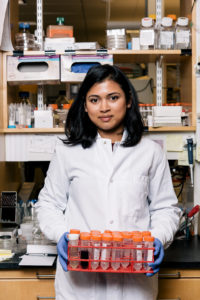 Graduate student holds a case of vials in a lab.