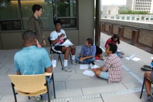 Students sit together outside with pencils and paper