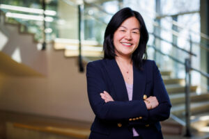 Evelyn Wang stands with arms folded in a dark blue blazer and lilac-colored top