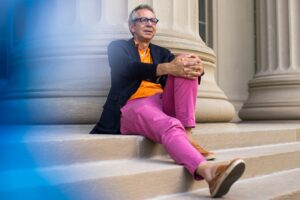 Photo of Peter Fisher sitting on the steps of an MIT building, leaning against a large column