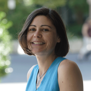 Headshot of a woman standing outside in a blue sleeveless top.