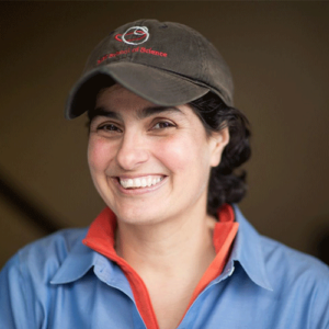 Headshot of woman in gray baseball cap, blue  button down shirt.