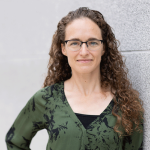 Headshot of a woman standing outside in a green long-sleeved top.