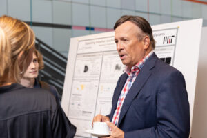 Frank Laukien stands in front of a presentation poster speaking to Professor Katharina Ribbek