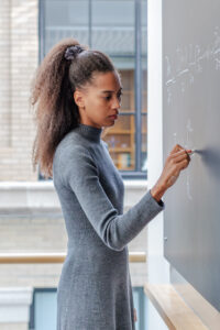 MLK Visiting Scholar and postdoc, Morgane König, faces a chalkboard and write the gravitational Komaneets equation to describe her cosmology research.