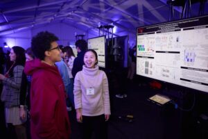 students smile and look at a poster about breast cancer research during the MIT HEALS launch