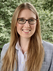 A white woman with blonde hair and glasses stands outside in a button-down shirt